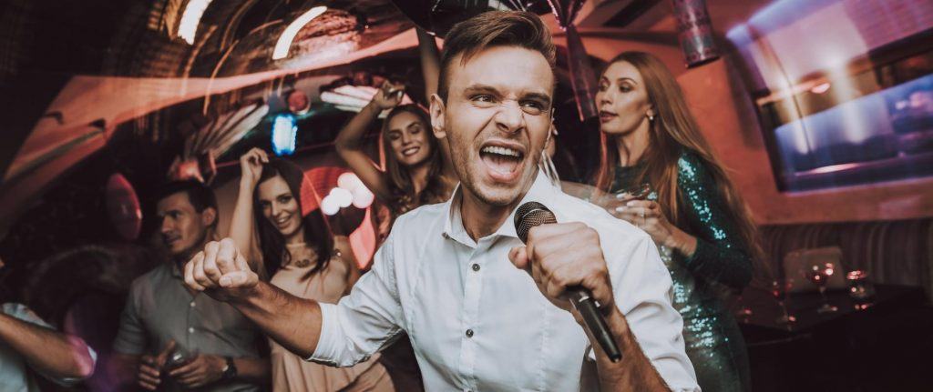 Man in white shirt singing karaoke at a party with friends in the background