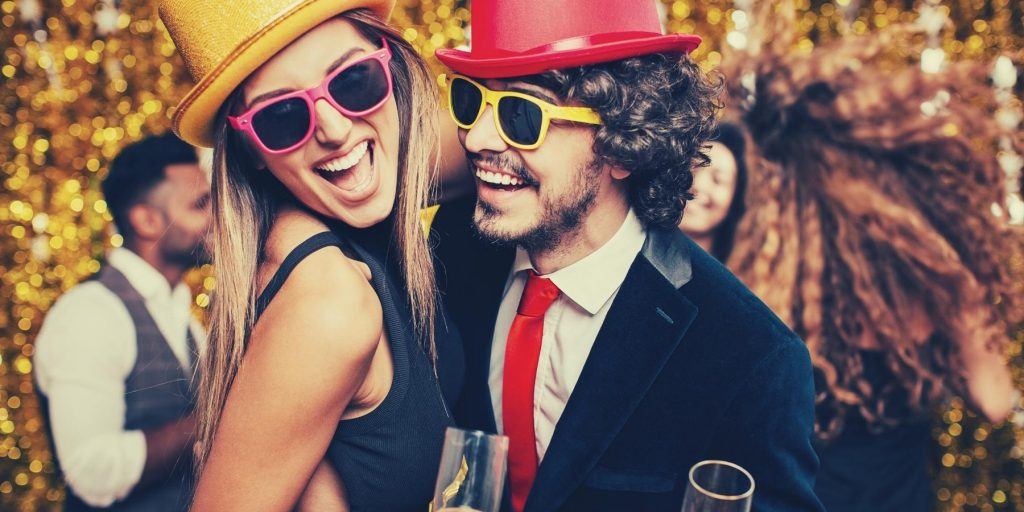 Front shot of a laughing woman and man wearing colorful sunglasses and hats