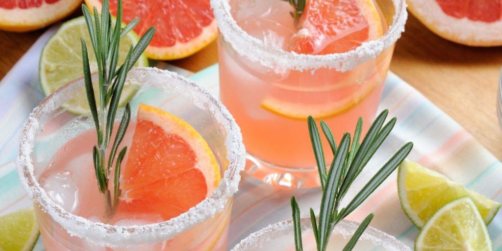 Overhead shot of two Paloma cocktails garnished with fresh grapefruit slices and sprigs of rosemary