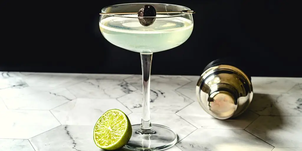 Close-up of a Last Word Cocktail garnished with a brandied cherry on a marble surface against a dark backdrop