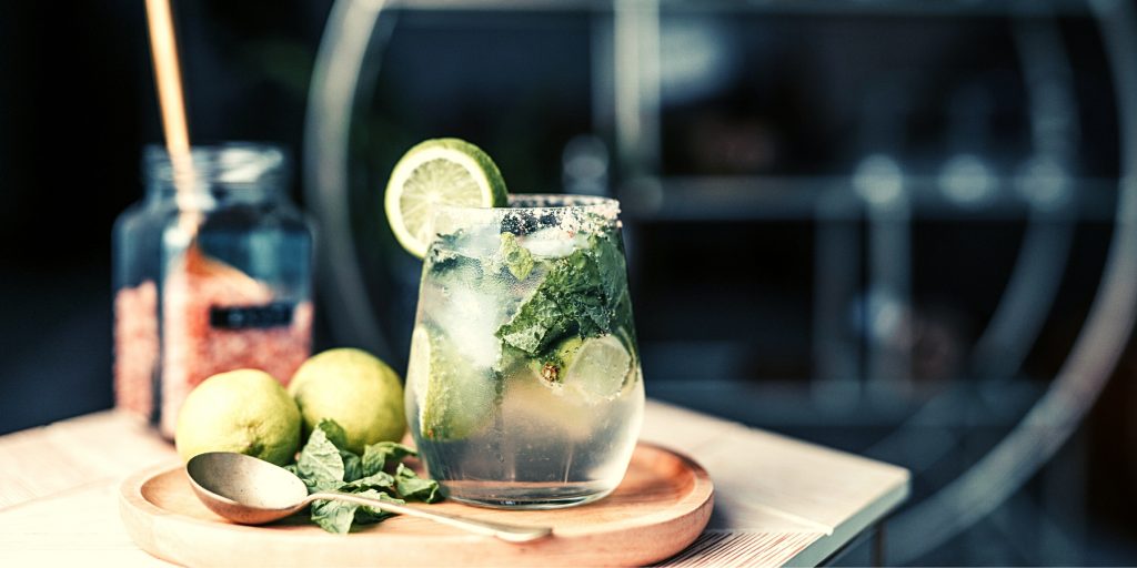 Front view of a refreshing Mojito cocktail with mint leaves and lime wedges on a wooden serving platter against a dark backdrop