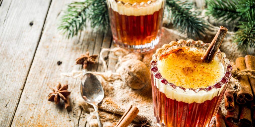 Two Hot Buttered Rum cocktails in mugs, garnished with a cinnamon stick each 