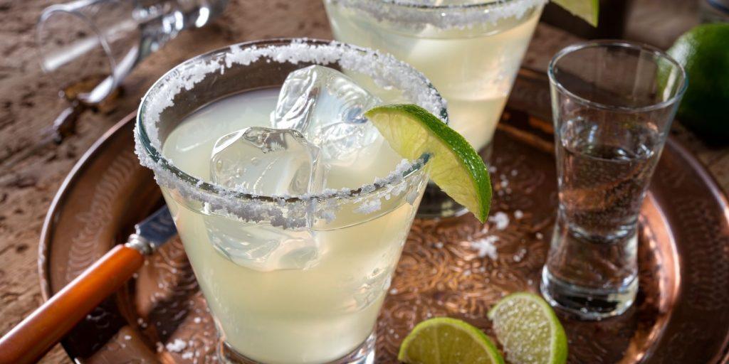 Close up top view of a pair of Cadillac Margarita cocktails with salted rims and lime wedges as garnish, on a copper serving platter