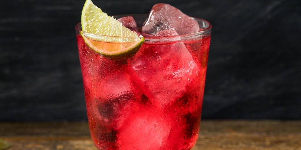 Close up front view of a Tutti frutti cocktail with cranberry juice and melon liqueur and a wedge of lime as garnish