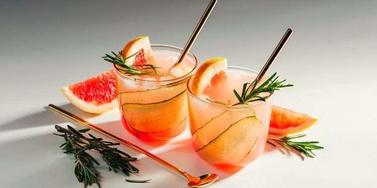 Two grapefruit and cucumber gin cocktails on a white background