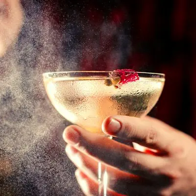 Mixologist spritzing bitters over a fancy summer cocktail