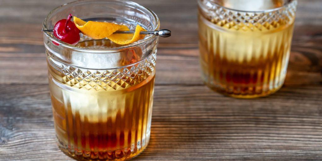 Close up front view of a pair of Old fashioned cocktails with cherry and orange peel garnish in rocks glasses on a wooden surface