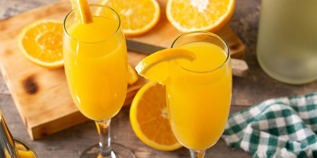 Close up top view of a pair of Mimosa cocktails with sliced oranges on a wooden cutting board behind it