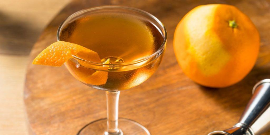 Close up top view of a boozy Classic Hanky Panky Cocktail in coupe glass on a wooden surface with a fresh orange and metal cocktail jigger to the side