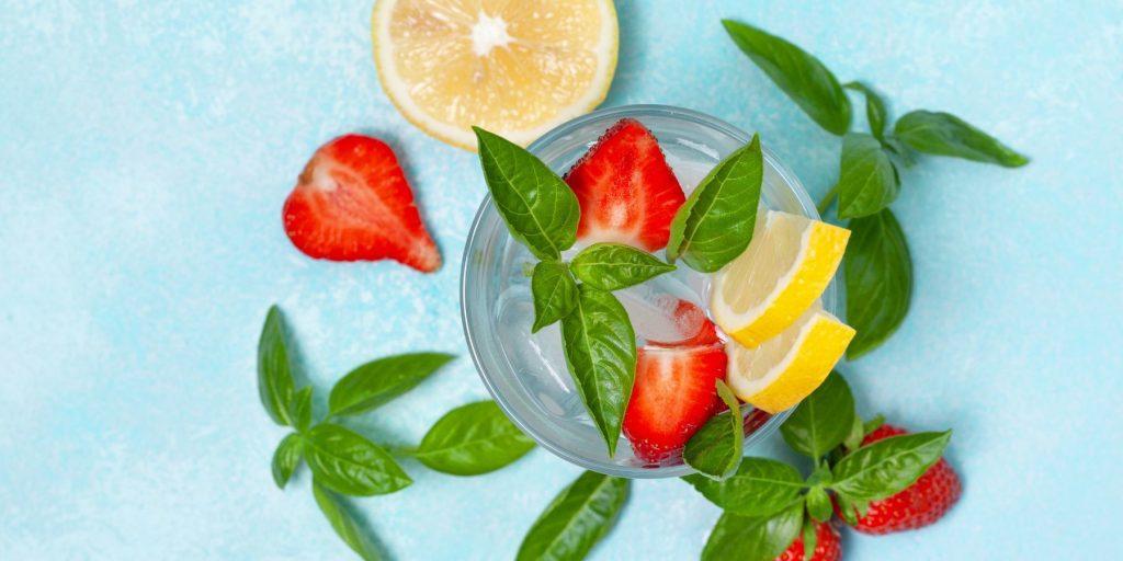 Top View of Strawberry Basil Cocktail garnished with fresh strawberries, basil and lemon slices on a light blue surface