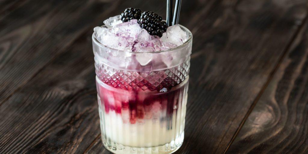 Close up of a creamy Apple and Elderflower Dream garnished with Blackberries on a dark wooden surface