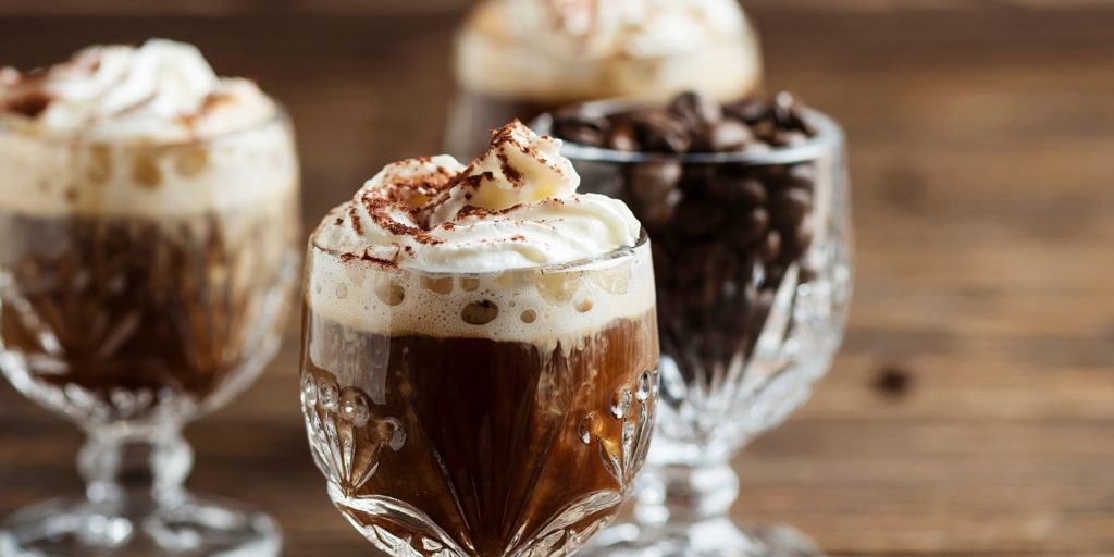 Close up front view of a trio of Hot Mexican Coffee Cocktails in cut-glass tumblers with cream and cocao as garnish