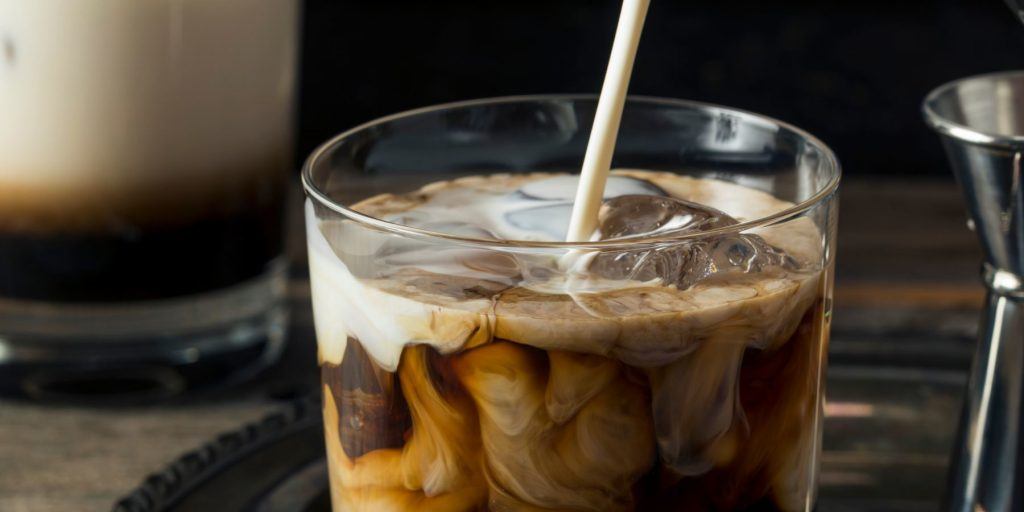 Close up image cream being poured into a dreamy White Russian cocktail, with another White Russian visible in the background