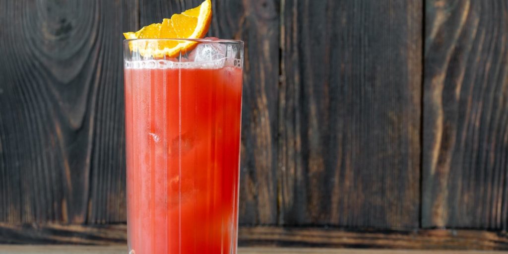 Front view of a Garibaldi Cocktail against a grey wooden backdrop, garnished with an orange wedge