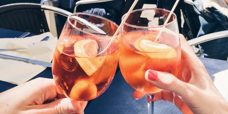Two hands clinking Aperol Spritz together