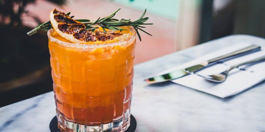 Close up front view of a Blood Orange Margarita garnished with a dehydrated slice of grapefruit and a sprig of rosemary