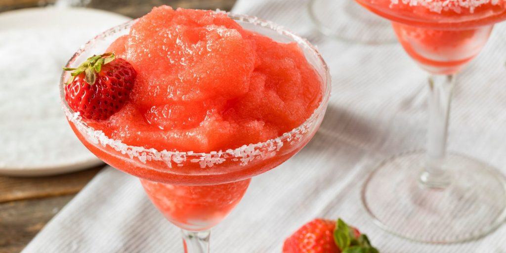 Close up of a two Frozen Strawberry Daiquiris with sugar rims and fresh strawberries as garnish