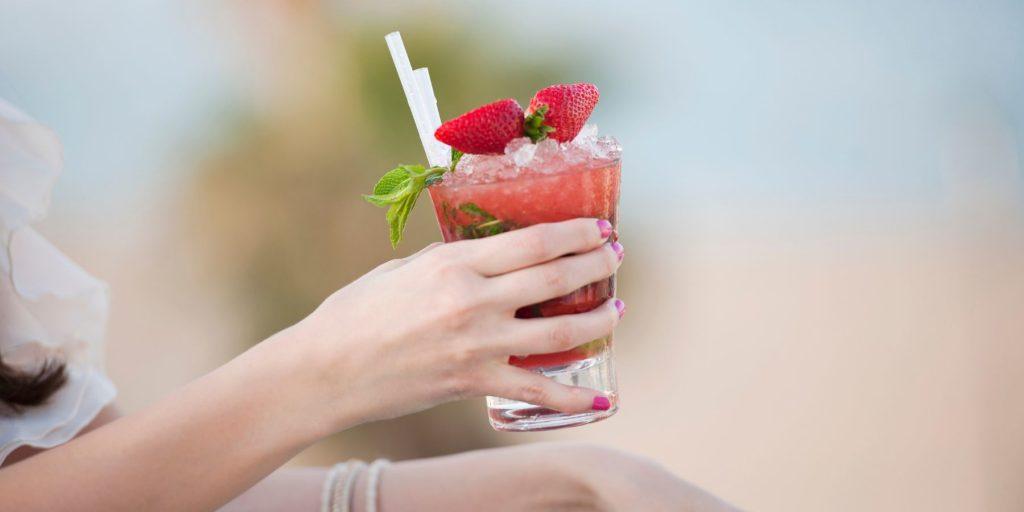 Woman's hand with pink nails holding a Strawberry Daiquiri with strawberry garnish