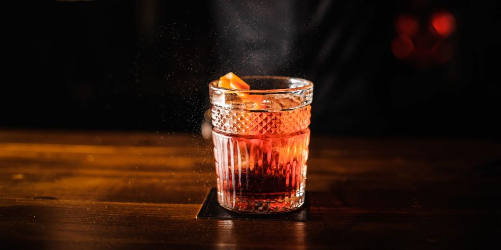 Close up of a 1789 cocktail on a dark wooden counter against a black backdrop