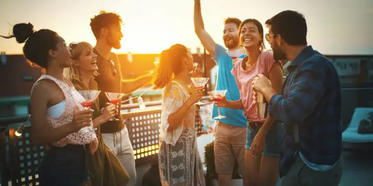 A group of diverse friends having a great time at an outdoor cocktail party hosted on a rooftop at dusk