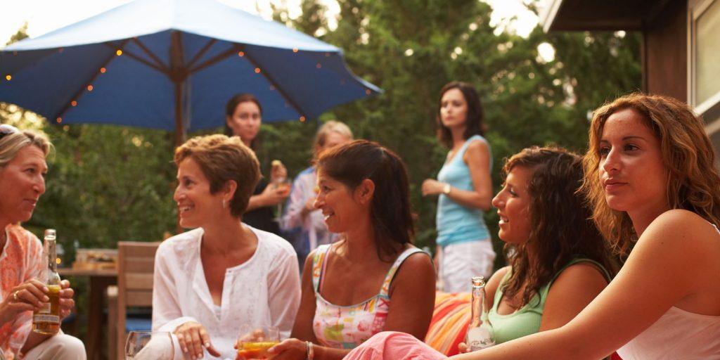 Group of women chatting and smiling next to an umbrella set up as a shade solution for an outdoor cocktail party