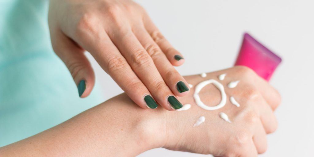 Close up of a woman with green nails applying sunscreen from to her hand from a pink tube