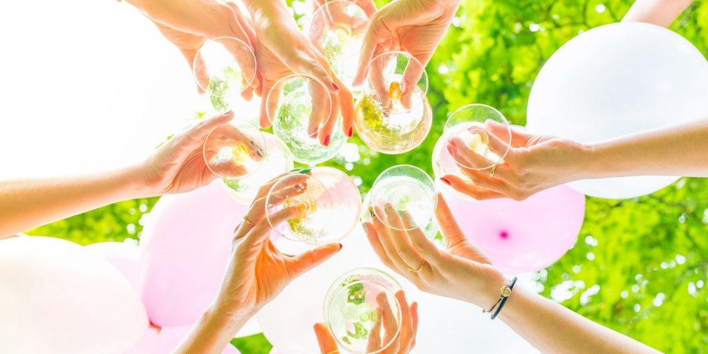 Bottom view of eight friends' hands clinking cocktails at a hen do with greenery visible above
