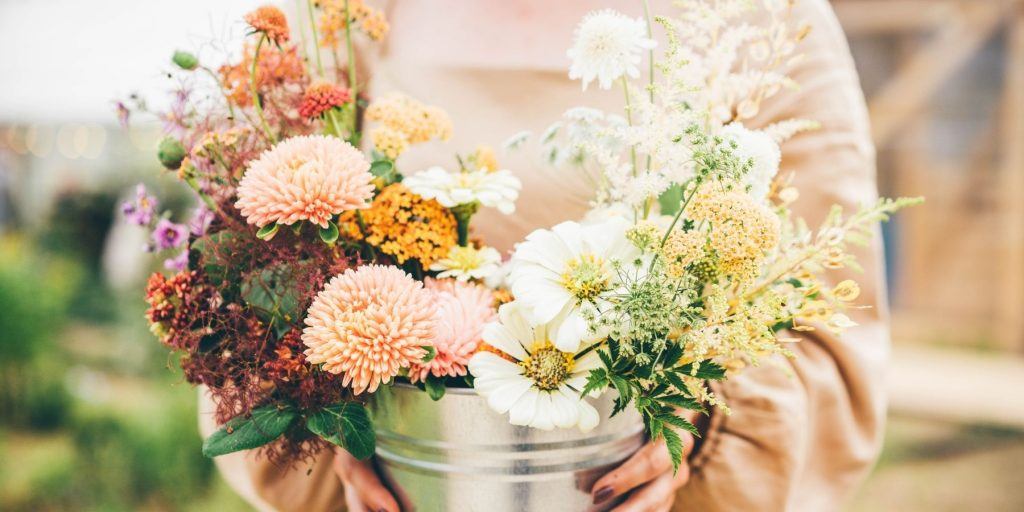Close up of a person in a soft pink jumper holding a pretty bucket full of flowers that have been compiled as decorations for a bachelorette party