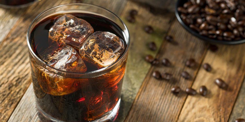 Close-up top view of a Black Russian Cocktail on the rocks, on a wooden surface, scattered with coffee beans