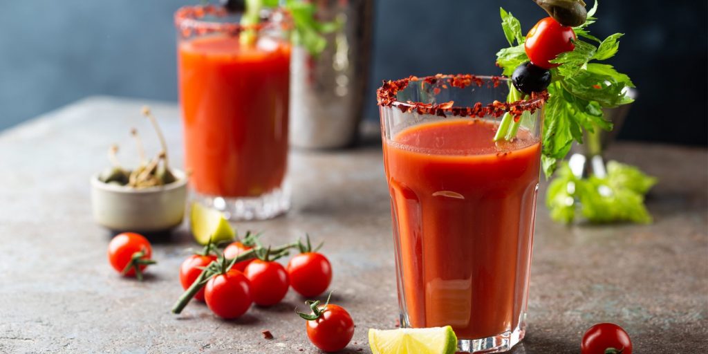 Close up front view of a pair of Virgin Mary Mocktails on a grey surface, garnished with totmatoes, olives and celery