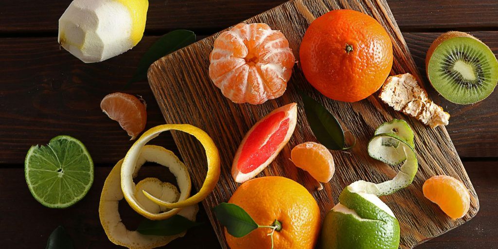 Top view of a selection of peeled and sliced citrus fruit on a wooden chopping board, including clementines, lemons and kiwi
