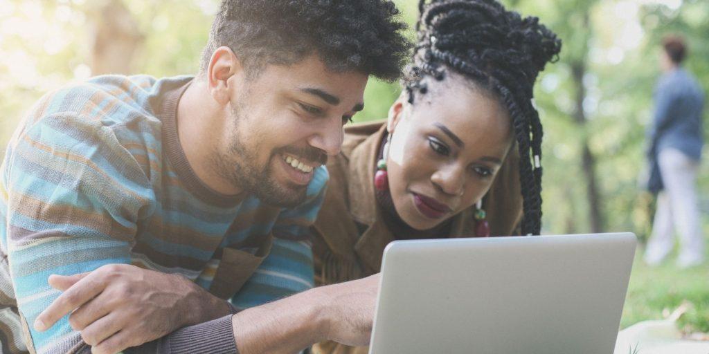 Close up of a smiling couple outdoors, looking at a laptop screen, planning a birthday party