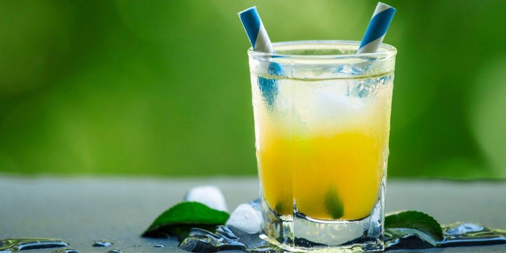 Close up front view of a refreshing Screwdriver cocktail on a grey surface with greenery in the background