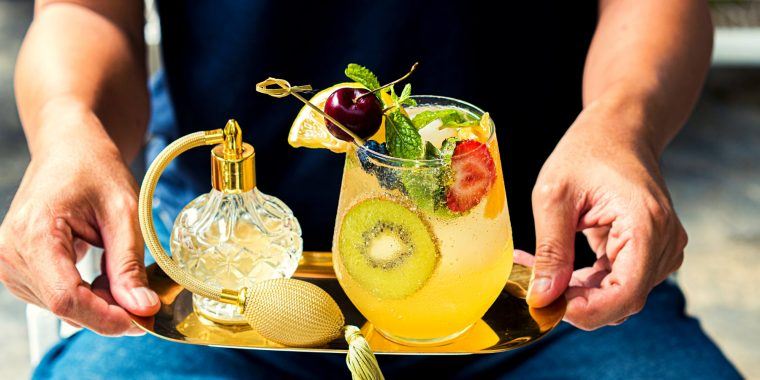 Close up front view of a fruity Kiwi and Mint Mocktail held on a golden-hued serving tray by a server in a black short-sleeve shirt