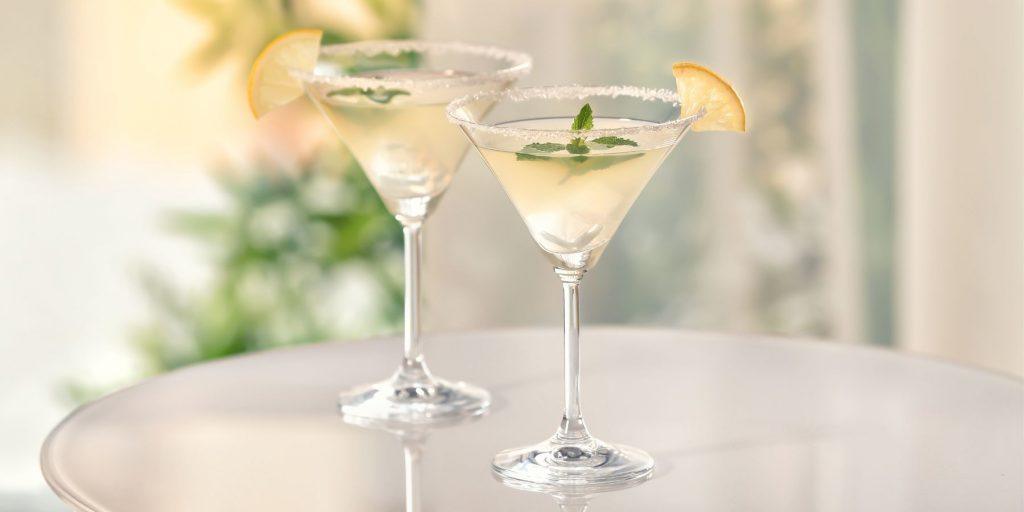 Two pretty Lemon Drop Martinis on a glass table, garnished with a sugar rim each