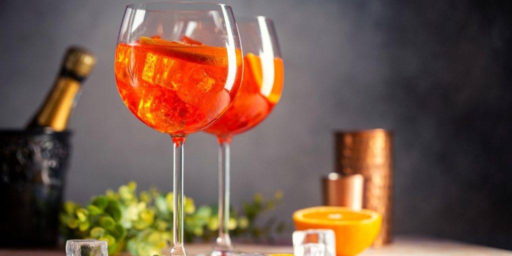 Three Aperol Spritz cocktails in wine glasses garnished with orange slices, viewed from the front, with Christmas trimmings in the background.