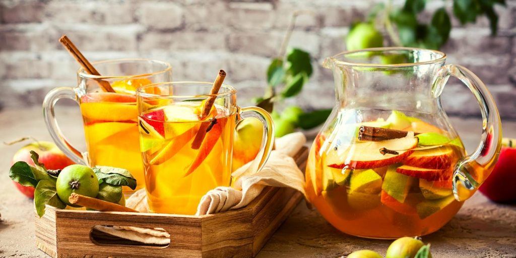 Jug of Apple Cider Sangria with garnished mugs on a tray