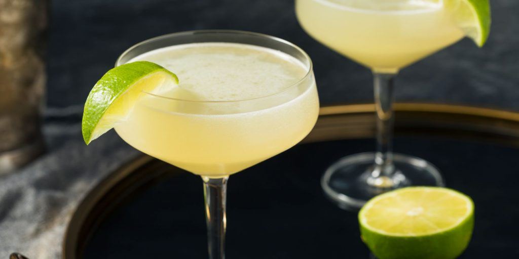 Close up of a pair of classic Gimlet cocktails garnished with lime wedges on a dark serving tray rimmed in gold