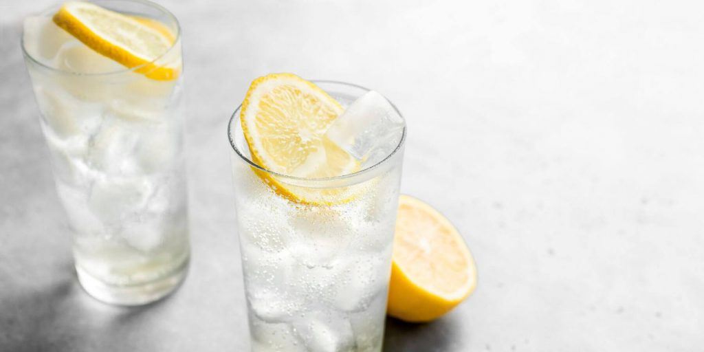 Close up top view of two Tom Collins cocktails on a white background with lemon