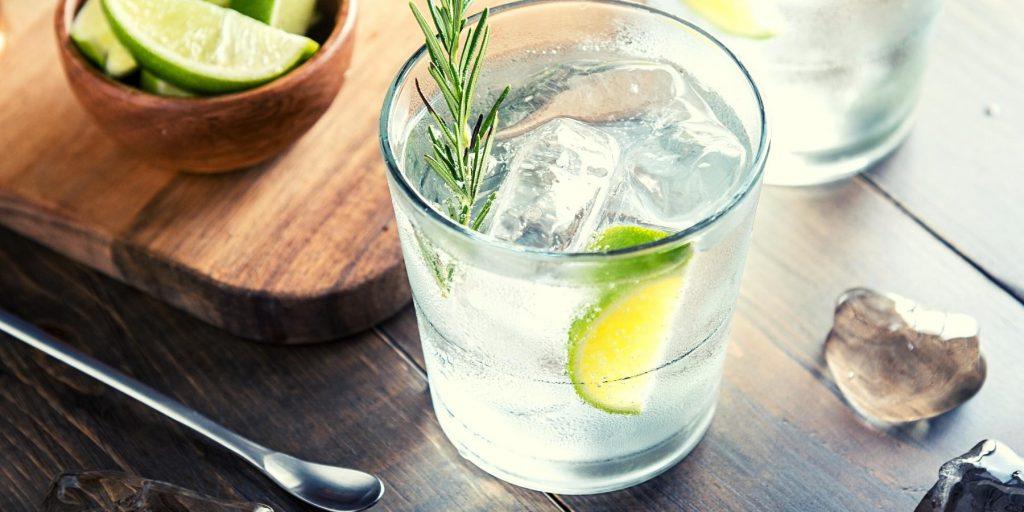 White rum with tonic water on ice with lime and rosemary garnish