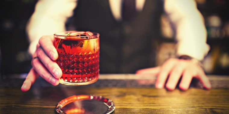Bartender serving a bright red Negroni cocktail