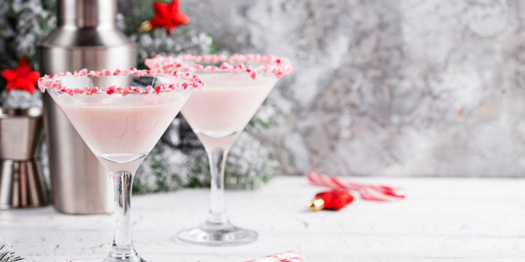 Two Peppermint Martinis with candy rims against a snowy backdrop with Christmas decorations to the side