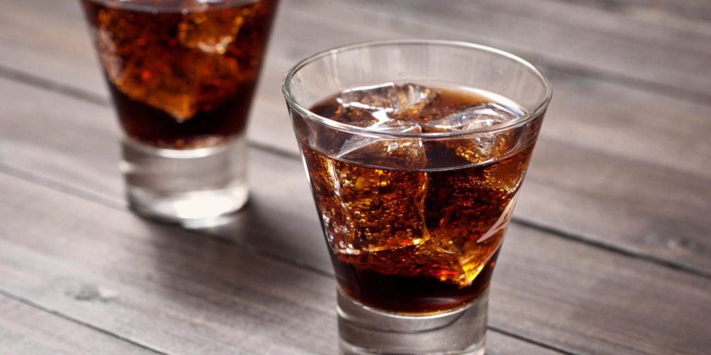 Close up of two Vodka & Dr Pepper cocktails in rocks glasses on a wooden surface