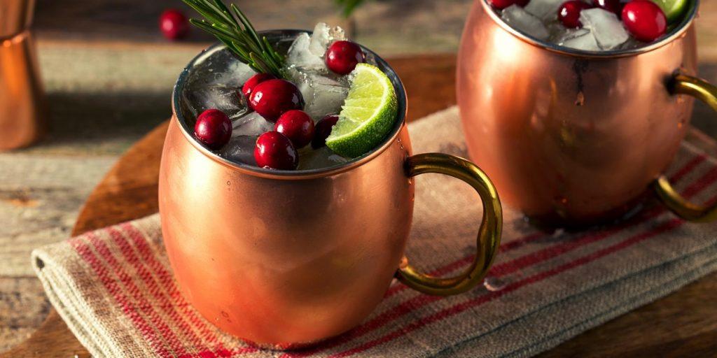 Refreshing festive Moscow Mule cocktails in copper mugs with lime and cranberry garnish