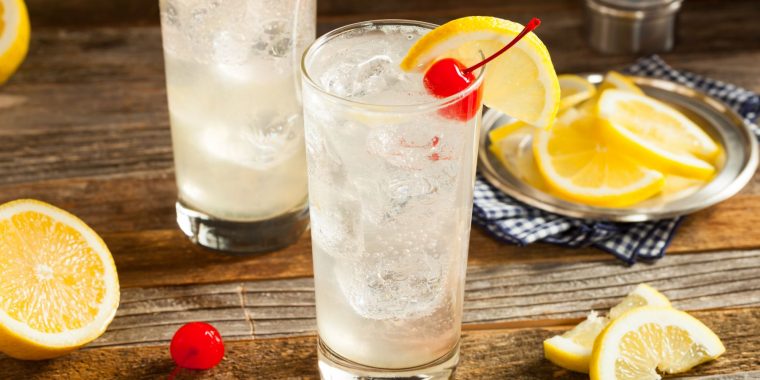 Two refreshing Tom Collins cocktails on a wooden surface, garnished with lemon slices and cherries