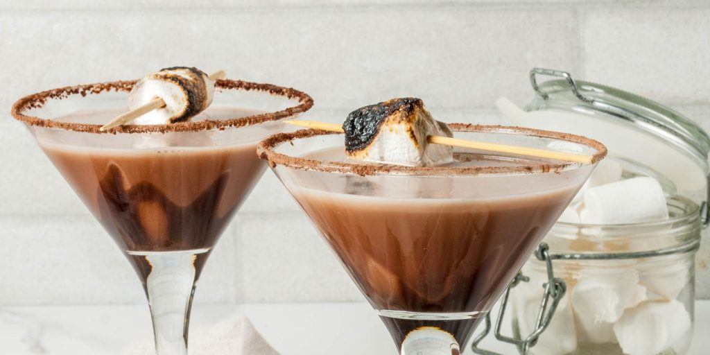Two creamy S'mores Martinis in Martin glasses, garnished with chocolate rims and toasted marshmallows against a white backdrop