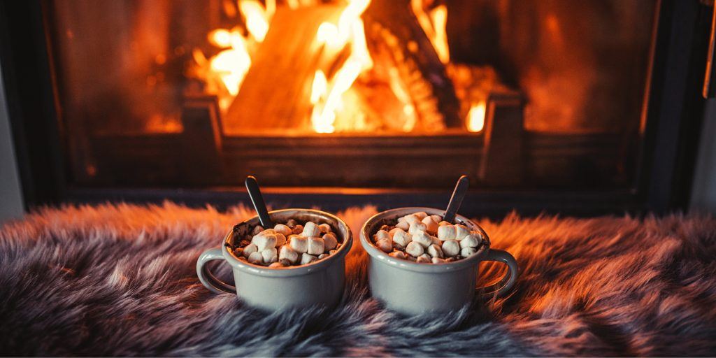 Two Toasted Marshmallow Campfire Mocktails on a shaggy blanket in front of a roaring fire