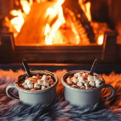 Two Toasted Marshmallow Campfire Mocktails on a shaggy blanket in front of a roaring fire