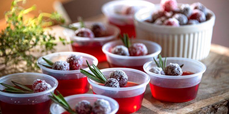 A tray of red Jello Shots garnished with berries and rosemary