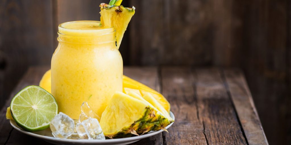 Creamy Bahama Mama cocktail served in a mason jar style glass, on a small plate surrounded by fresh limes and pineapple slices on a wooden surface